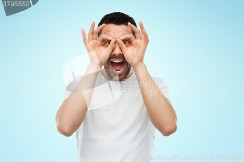 Image of man making finger glasses over blue background