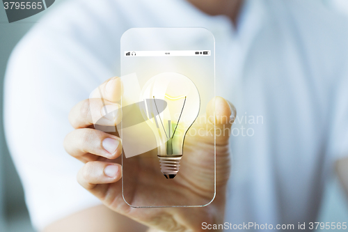 Image of close up of hand with light bulb on smartphone