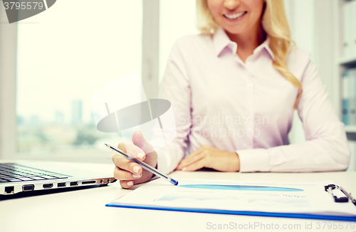 Image of smiling businesswoman reading papers in office