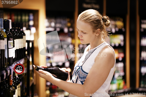 Image of Woman reading inscription on the wine bottle in store