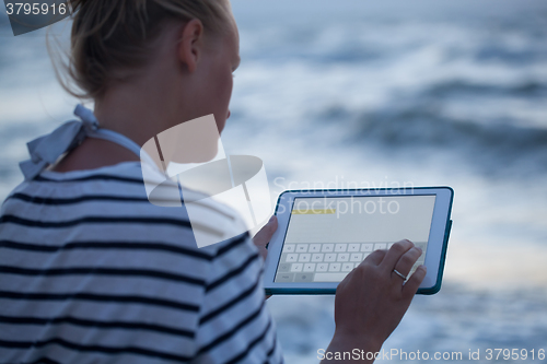 Image of Woman typing on tablet PC by sea