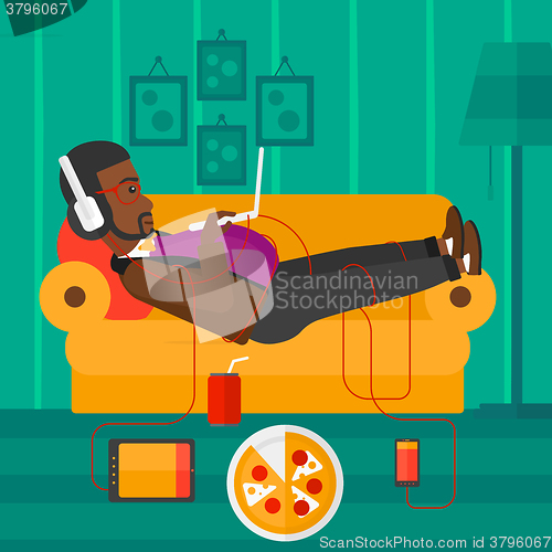 Image of Man lying on sofa with many gadgets.