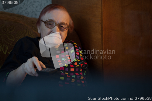 Image of Old woman at home watching TV and changing channels