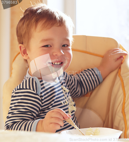 Image of Two year old boy smiles and eating porridge.
