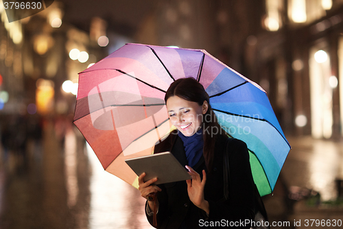 Image of Woman using pad under umbrella in the evening city