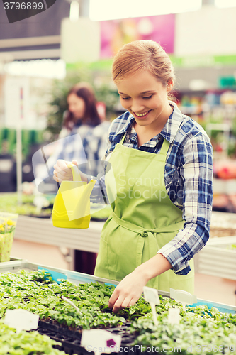 Image of happy woman with watering can in greenhouse