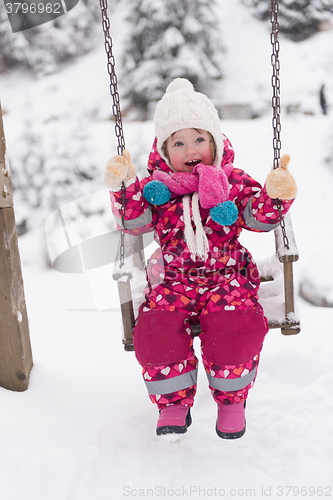 Image of little girl at snowy winter day swing in park