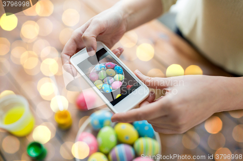 Image of close up of hands with easter eggs and smartphone