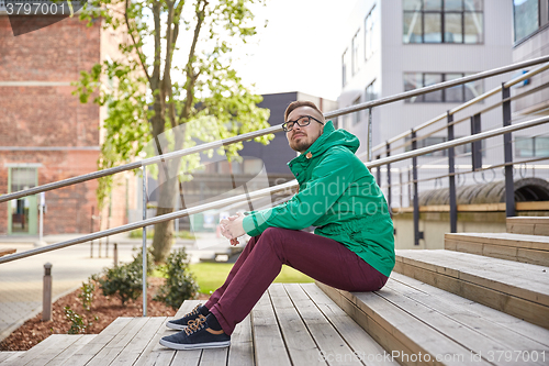 Image of happy young hipster man sitting on stairs in city