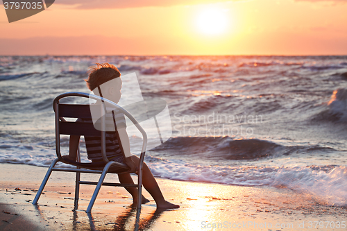 Image of Little child looking at sunset sitting by the sea