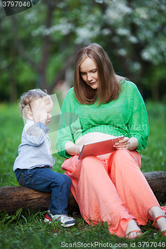 Image of Pregnant mother with little son using touch pad in the park