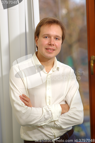 Image of Happy young man standing by the window with blinds