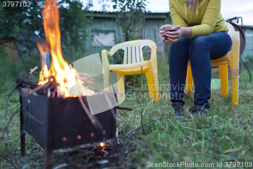 Image of Woman with tea near the fire in yard