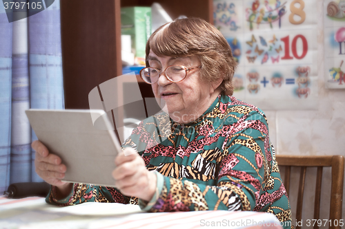 Image of Elderly woman in glasses watching something on pad