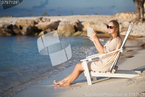 Image of Woman with pad relaxing in chaise-lounge on the beach