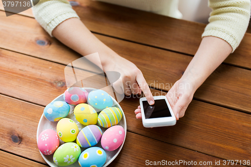 Image of close up of hands with easter eggs and smartphone