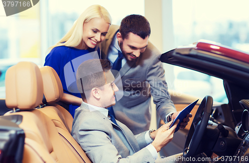 Image of happy couple with car dealer in auto show or salon