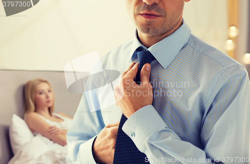 Image of close up of man adjusting tie on neck in bedroom