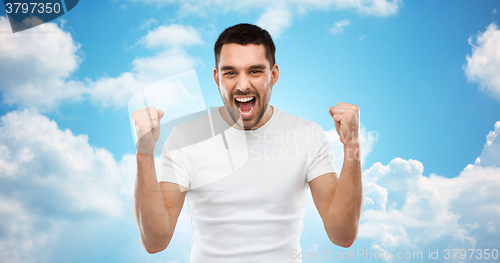 Image of young man celebrating victory over blue sky