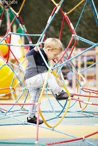 Image of Happy little boy climbing on playground equipment