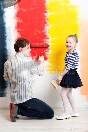 Image of Happy girl painting wall with father