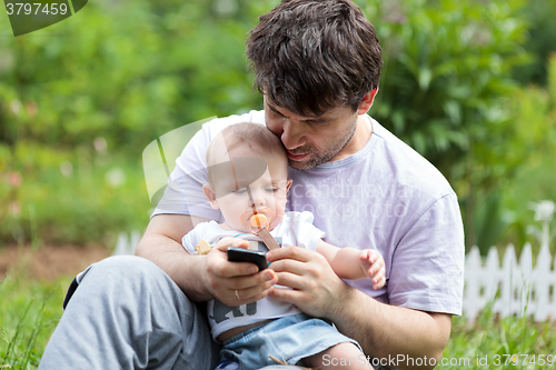 Image of Father holding a baby and texting on his mobile