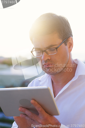 Image of Young businessman deep at work with pad outdoor