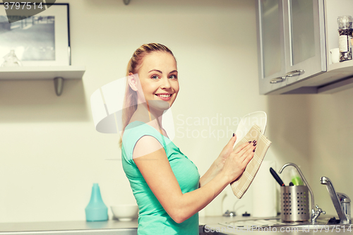 Image of happy woman wiping dishes at home kitchen