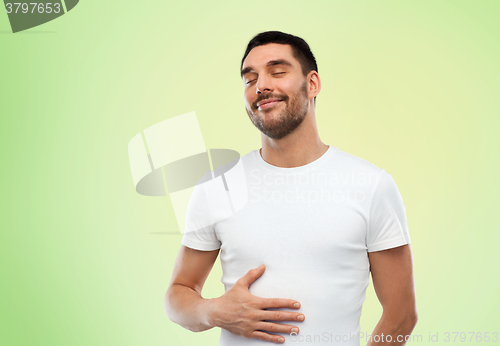 Image of happy full man touching tummy over green 