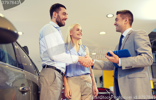 Image of happy couple with car dealer in auto show or salon