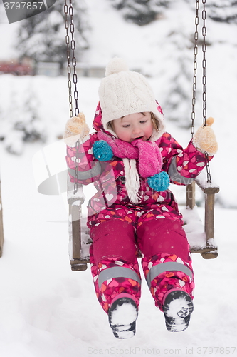 Image of little girl at snowy winter day swing in park