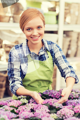 Image of happy woman taking care of flowers in greenhouse