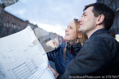 Image of Couple holding blueprints admiring building