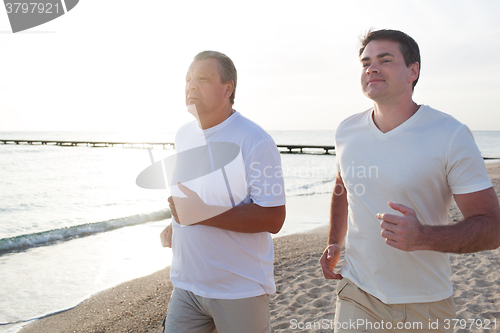 Image of Two men running along the coast in bright sunlight