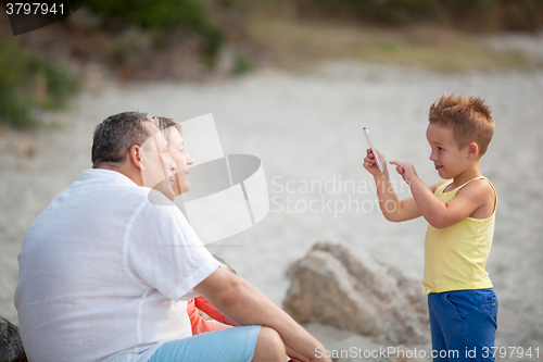 Image of Boy taking phone photo of grandparents outdoor