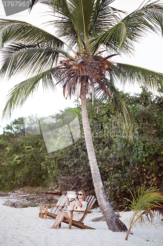 Image of Woman relaxing under palm and making photos with pad