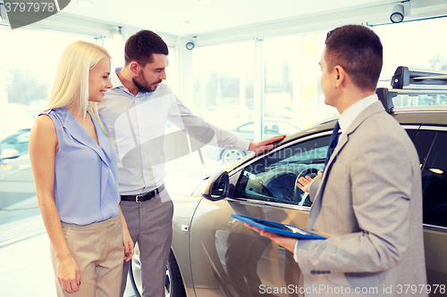 Image of happy couple with car dealer in auto show or salon