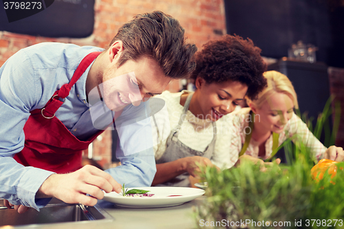 Image of happy friends cooking and decorating dishes