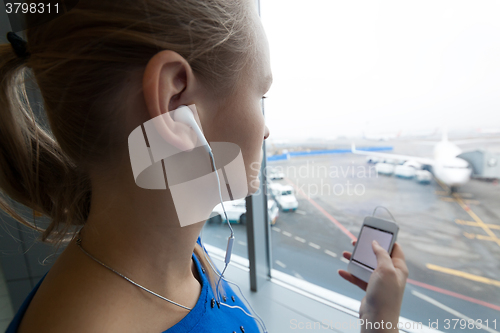 Image of Woman listening to music by the window at airport