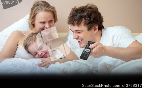 Image of Happy family lying in bed watching television