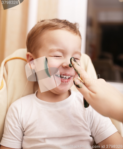 Image of Little boy laughing as his mother paints his face