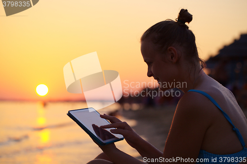 Image of Smiling woman using pad on beach at sunset