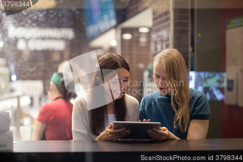 Image of Two women talk cheerfully in the restaurant using electronic tablet