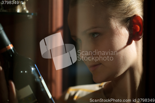 Image of Woman taking a bottle of wine from liquor cabinet