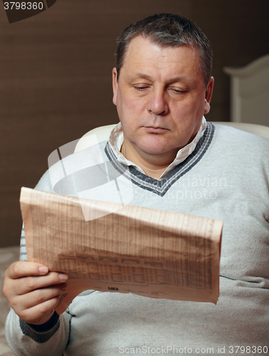 Image of Portrait of senior man reading newspaper at home.