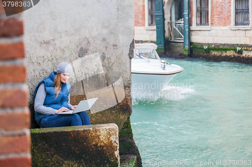 Image of Young woman using laptop by the canal in Venice