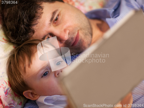 Image of Man and little boy playing with tablet in bed