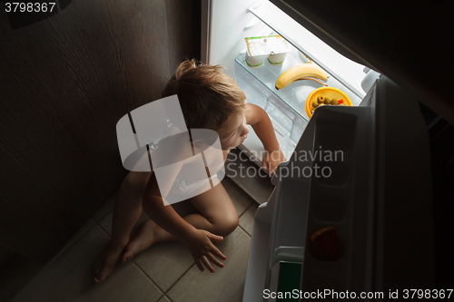 Image of Little boy sitting near open fridge at night