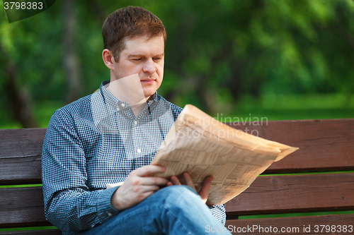Image of Man reads newspaper on bench in the park