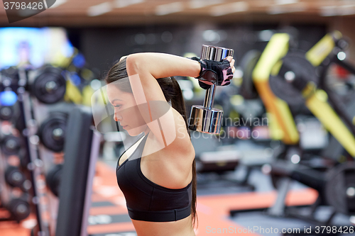 Image of young woman flexing muscles with dumbbell in gym